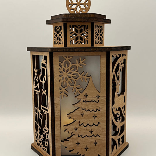 A hexagonal wooden lantern with laser-cut winter motifs including a Christmas tree, snowflakes, and a reindeer, shown on a neutral light gray background.
