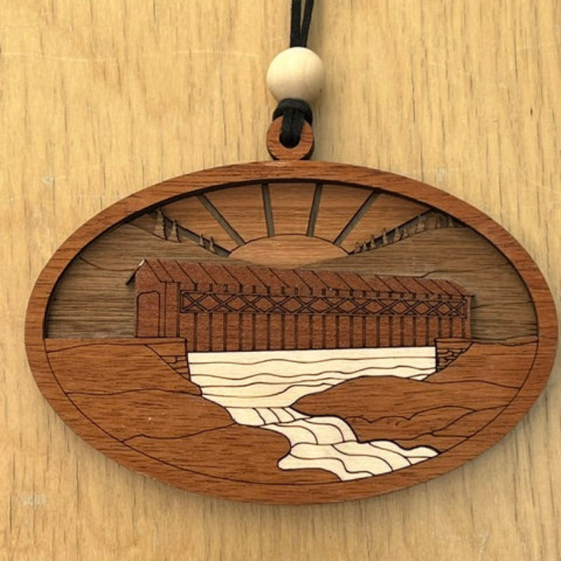 Wooden pendant with intricate engraving of a covered bridge on a wooden surface