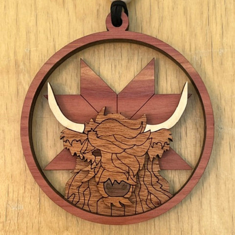 Wooden pendant with geometric design behind an engraved highland cow on a wooden surface