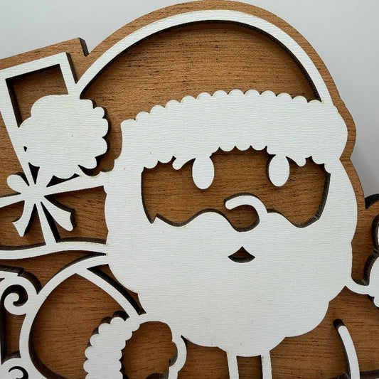 A close-up of a wooden Santa Claus cutout decoration, showing a white-painted face and beard silhouette over a natural brown wood background.