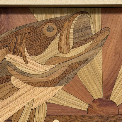 Close-up of a wooden fish inlay artwork made from multiple wood tones, with a sunburst design in the background.