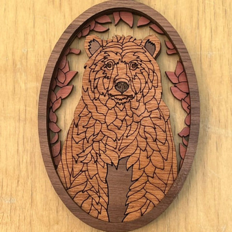 Wooden pendant with laser-cut design of a bear on a wooden surface