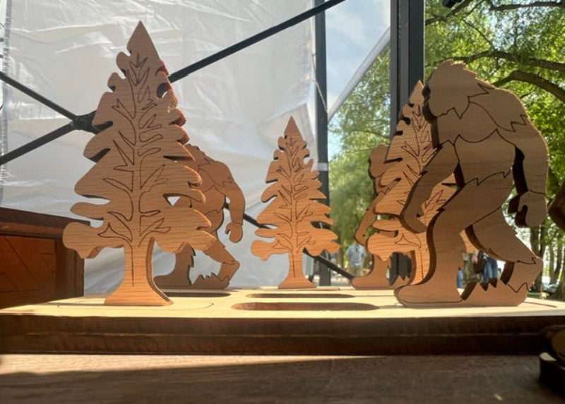 Wooden cutouts of trees and bigfoot tic tac toe game on a wooden surface 