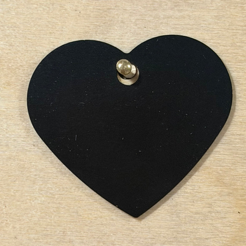 Black metal dog tag heart shaped hanging on a light wood background