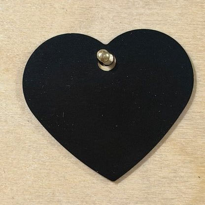 Black metal dog tag heart shaped hanging on a light wood background