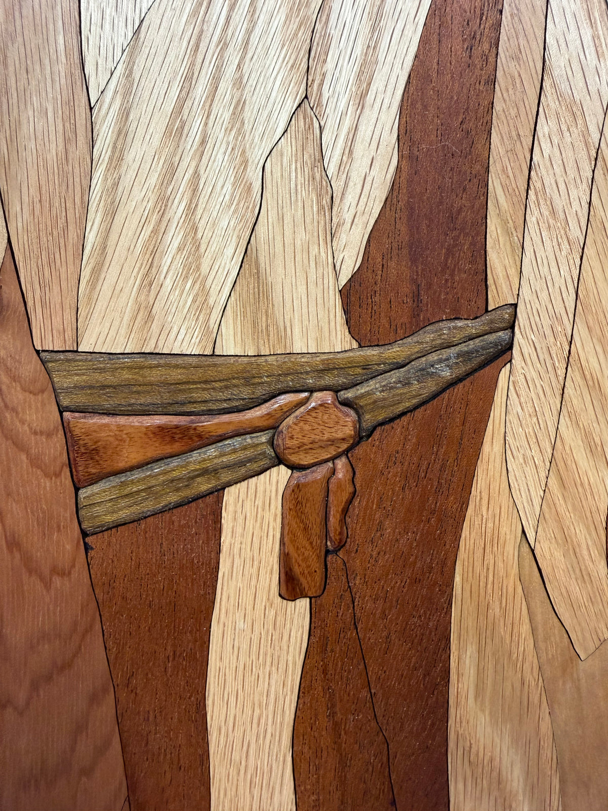Close-up of a wooden inlay or marquise design featuring varied wood tones including light tan, medium brown, and dark reddish-brown, with a central knot-like detail and diagonal wood strips.