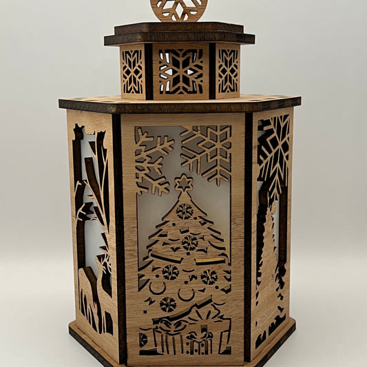 A hexagonal wooden lantern with laser-cut Christmas tree, snowflakes, and winter landscape designs on a light gray background.