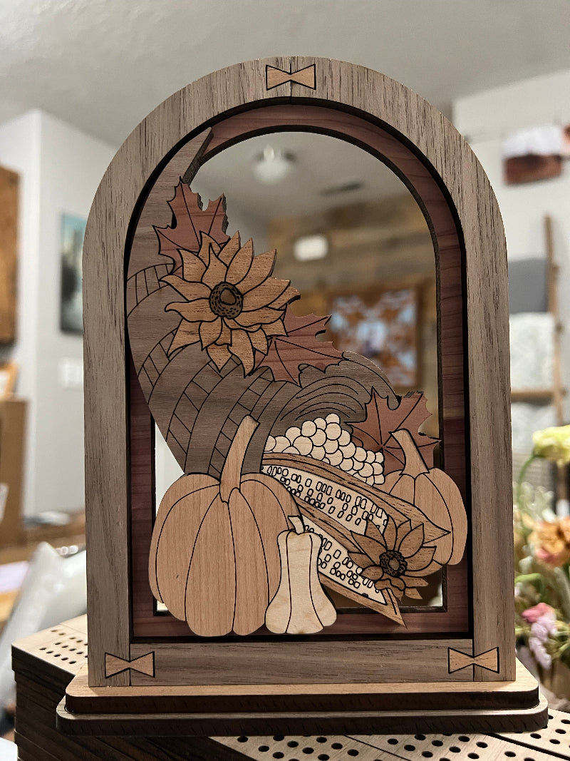 Wooden Cornucopia in multiple woods within an arched frame. Designed to sit on a shelf