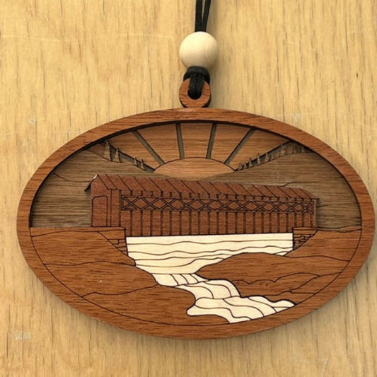 Wooden pendant with intricate engraving of a covered bridge on a wooden surface