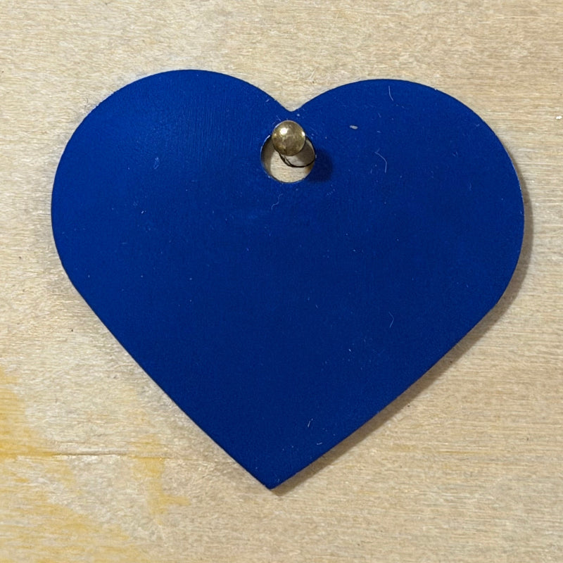 A heart-shaped blue metal tag hanging on a light wood background.