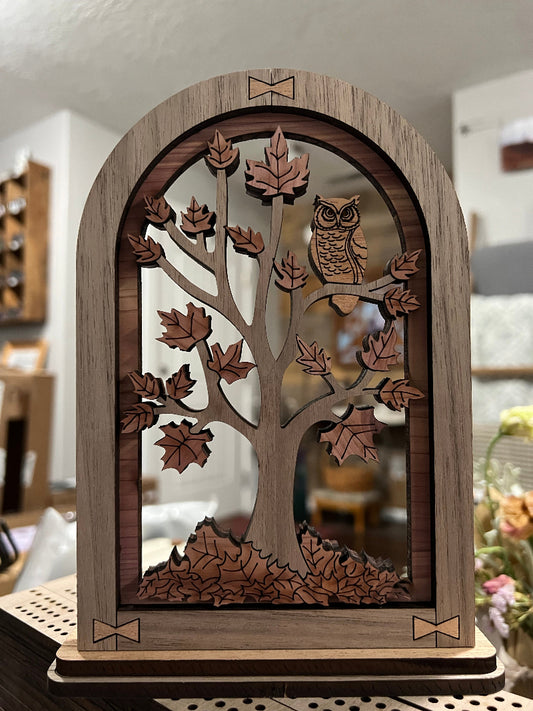 Wooden decorative item with cut-out design of leaves and an owl in an arched frame designed to sit on a table