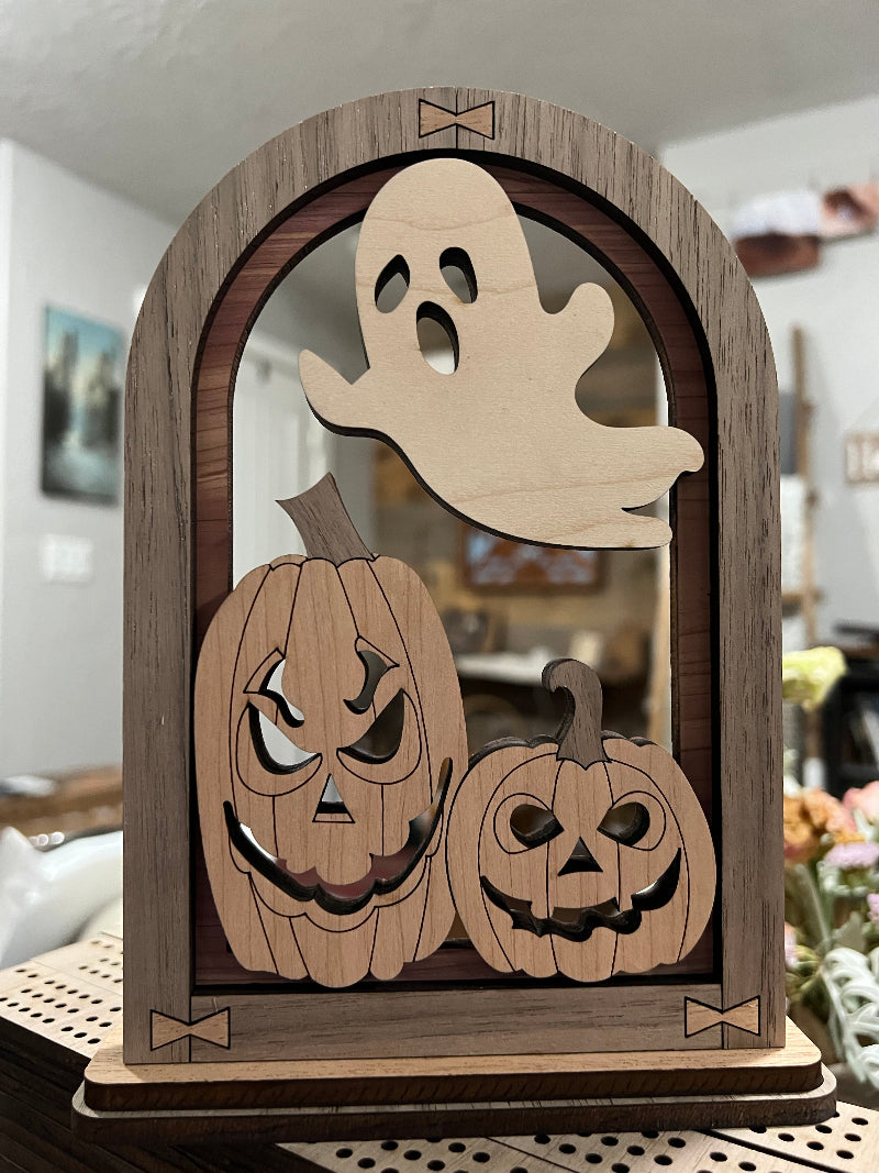 Wooden Halloween decoration including pumpkins and a ghost on a wooden board.