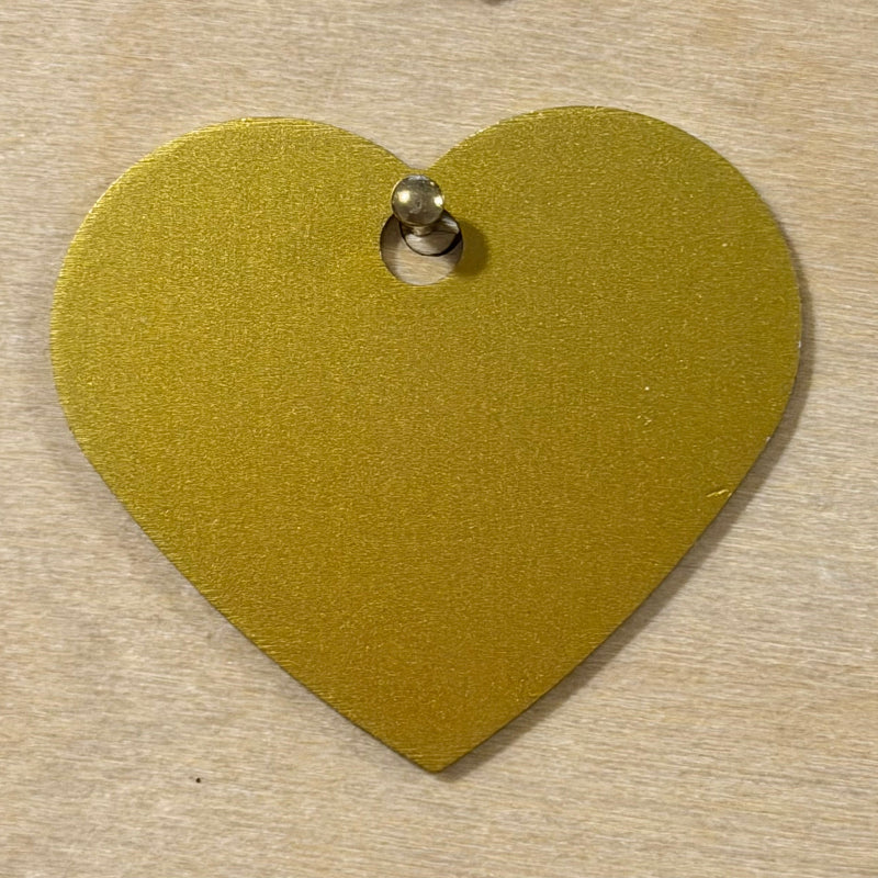 A gold heart-shaped metal tag with a small hole at the top, shown on a light wood background.