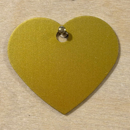 A gold heart-shaped metal tag with a small hole at the top, shown on a light wood background.