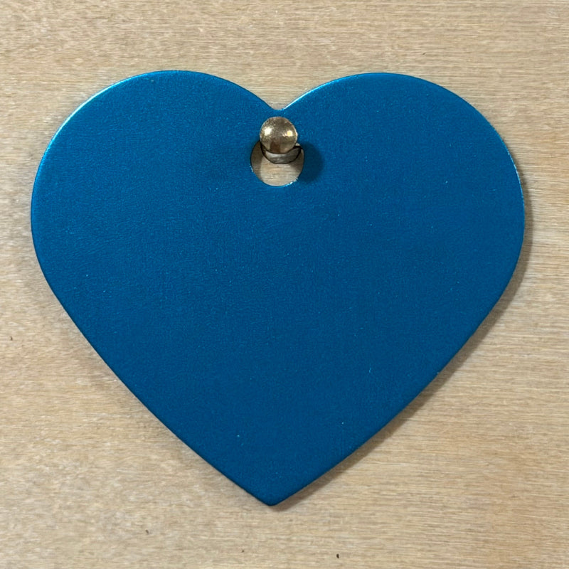 A light blue metal heart dog tag hanging on a light wood background