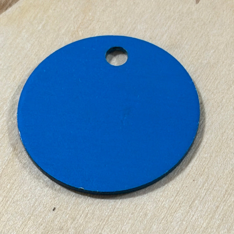 A round blue tag or label with a small hole near the top, placed on a light wood surface.