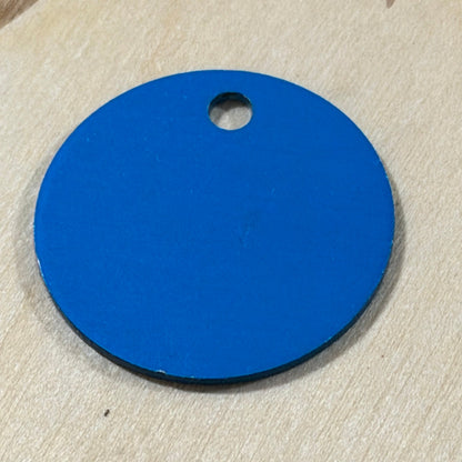 A round blue tag or label with a small hole near the top, placed on a light wood surface.