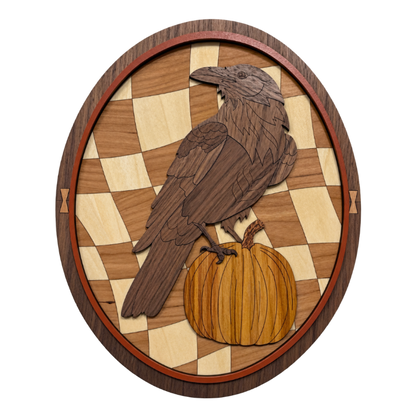 Oval wooden wall art featuring a laser cut raven perched on a pumpkin over a checkerboard background, shown on a plain white background.