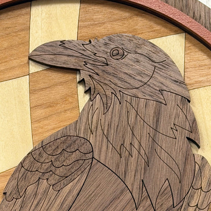 Close-up of a carved wooden raven or crow figure with engraved line details, set against a light wood checkerboard background.