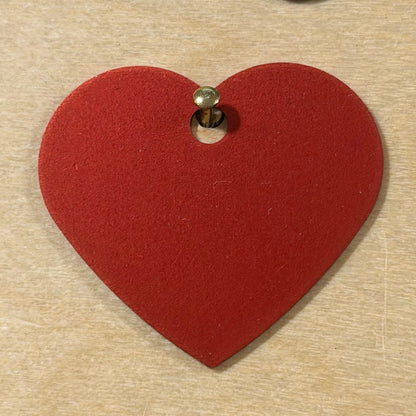 A red heart-shaped metal tag with a pre-drilled hole shown on a light wood background.