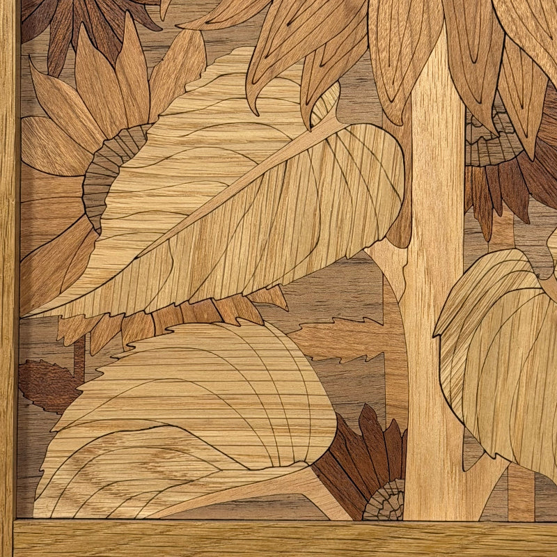 Close-up of a wooden inlay artwork featuring sunflowers and large leaves, crafted from natural wood tones with visible grain and a light wood border.
