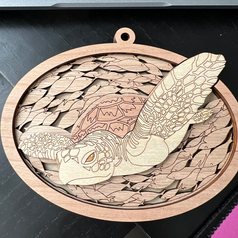 A laser-cut wooden sea turtle ornament with a hanging loop, displayed on a dark tabletop