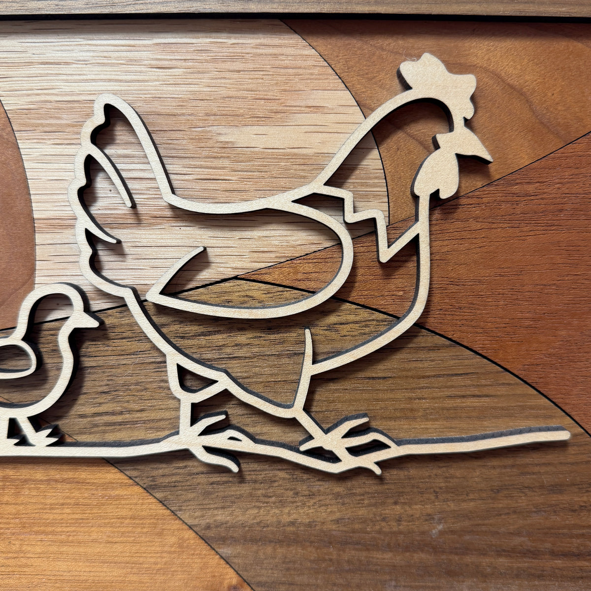 Detail of the layered maple hen and chick outline over the inlaid oak, cherry, and walnut backer