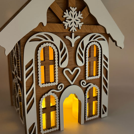 Front of the wooden gingerbread house lit up, mahogany with white MDF frosting overlays