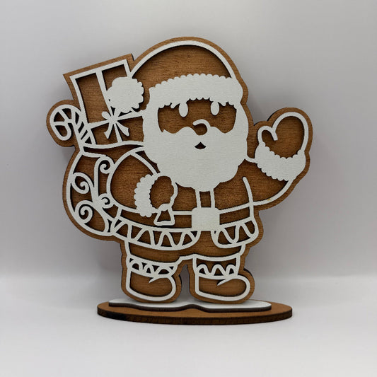 A laser-cut wooden Santa Claus tabletop decoration with a white outline and natural wood grain, standing on a small oval wooden base against a neutral gray background.