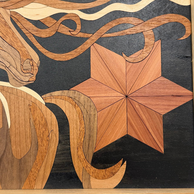 Close-up of an intricate wooden inlay artwork featuring a geometric eight-pointed star in warm medium brown wood, flowing ribbon-like shapes in light and dark brown, and a dark charcoal background.