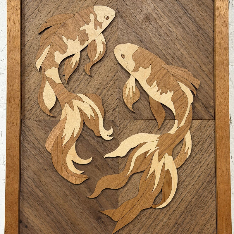 Intricately carved wooden wall art featuring two stylized koi fish in layered natural wood tones, mounted on a geometric wood panel with a simple wooden frame.