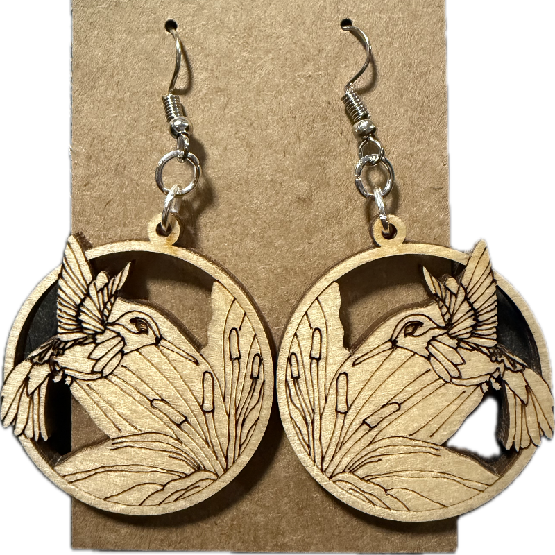A pair of wooden dangle earrings displayed on a brown kraft card. Each circular wooden earring features a laser-cut design of a bird in flight above reeds, with a silver-toned fishhook ear wire attached at the top.