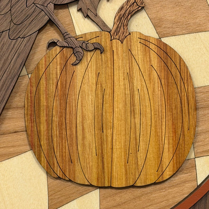 A close-up of a wooden pumpkin-shaped decorative piece with engraved wood grain and black line details, placed on a multicolor wood-patterned surface.