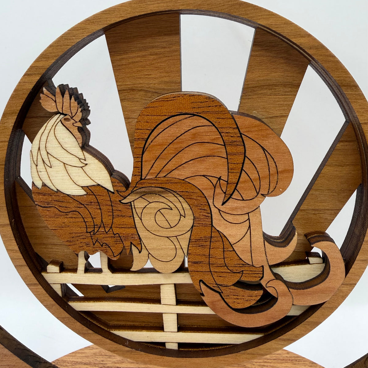 A circular wooden rooster figurine with layered laser-cut wood pieces in varying shades of brown and natural wood tones, set against a white background.