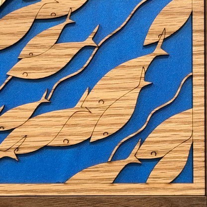 Close-up of a wooden wall art piece featuring layered fish cutouts in a natural wood tone over a bright blue background.
