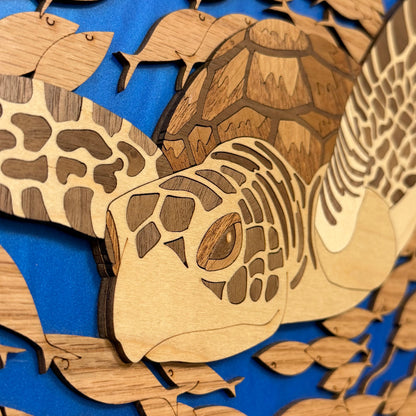 Laser-cut wooden sea turtle and fish wall art layered over a blue background, showing natural wood grain and cutout details.